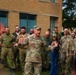 A U.S. Army officer with the name tape 'STUBBS' and four-star rank insignia is addressing a group of military personnel outdoors near a brick building. The assembled group includes soldiers in various camouflage uniforms, some with face paint applied, suggesting a recent or ongoing field exercise. The officer appears to be delivering a briefing or after-action remarks to a mixed multinational military audience.