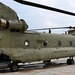 The image shows a United States Army CH-47 Chinook tandem-rotor heavy-lift helicopter parked on a tarmac or airfield. The aircraft is painted in standard olive drab/army green livery with 'UNITED STATES ARMY' markings visible on the fuselage. The rear cargo ramp appears to be lowered, and at least one soldier in camouflage uniform is visible near the aircraft.