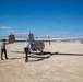 Two individuals are working with a small propeller-driven aircraft on a dry desert lakebed or airstrip under clear blue skies. The aircraft, bearing the registration number N53WP, appears to be a twin-boom pusher-configuration unmanned or light manned aircraft. A white SUV is visible in the background, and mountains line the distant horizon.