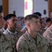 A group of U.S. Marines in MARPAT camouflage uniforms are seated in rows inside what appears to be a chapel or large assembly hall. They appear to be attending a formal ceremony or briefing, facing attentively in the same direction. Multiple rows of personnel are visible extending into the background.