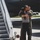 MAINEiacs Return Home Two individuals are embracing near the base of an aircraft boarding stairway on a tarmac. One person is wearing an olive green flight suit, suggesting a military or aviation context. The emotional embrace appears to be a reunion or farewell scene at an airfield.