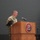 USARIEM COC/Relinquishment of Responsibility 2026 A U.S. Army officer in camouflage uniform is speaking at a podium bearing the USARIEM (U.S. Army Research Institute of Environmental Medicine) seal during an official military ceremony or event. Multiple flags, including the U.S. flag and military unit colors, are displayed to the right of the podium. The setting appears to be an indoor auditorium or ceremonial hall.
