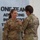 USARIEM COC/Relinquishment of Responsibility 2026 Two female U.S. Army soldiers in Operational Camouflage Pattern (OCP) uniforms are engaged in a military pinning ceremony. The soldier facing the camera, identified by the name tape 'ROSSER' and wearing a Colonel's eagle insignia, is receiving a pin or award from the other soldier. The ceremony is taking place indoors in front of a wall display reading 'ONE TEAM ADVANCING INNOVATIVE...'