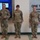 USARIEM COC/Relinquishment of Responsibility 2026 Three U.S. Army soldiers in OCP (Operational Camouflage Pattern) uniforms are standing in a formal indoor setting, likely during a military ceremony or presentation. The soldier on the left is holding what appears to be a folder or award certificate. They are positioned in front of a large display screen and a wall-mounted sign referencing innovation and technology.