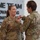 USARIEM COC/Relinquishment of Responsibility 2026 Two female U.S. Army soldiers in OCP (Operational Camouflage Pattern) uniforms are participating in a military award or decoration ceremony. One soldier, identified by her name tape as 'ROSSER,' is receiving a medal or pin being affixed to her uniform by the other soldier. The ceremony is taking place indoors in front of a wall display reading 'ONE TEAM ADVANCING INNOVATION TECHNOLOGY FOR...'