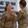 USARIEM COC/Relinquishment of Responsibility 2026 A military award ceremony is taking place indoors, where one uniformed soldier is pinning a medal or decoration onto another soldier named 'ROSSER' as indicated by the name tape on her uniform. Both individuals are wearing U.S. Army OCP (Operational Camouflage Pattern) uniforms. The background features a wall display with the text 'ONE TEAM ADVANCING INNOVATIVE TECHNOLOGY FOR...'