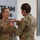 USARIEM COC/Relinquishment of Responsibility 2026 Two female U.S. Army soldiers in MultiCam/OCP camouflage uniforms are engaged in a military award or decoration ceremony. One soldier, identified by her name tape as 'ROSSER,' is receiving a medal or pin being affixed to her uniform by the other soldier. The ceremony appears to be taking place inside a military facility with motivational signage visible in the background.