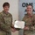 USARIEM COC/Relinquishment of Responsibility 2026 Two U.S. Army female soldiers are posing together while holding a certificate titled 'The Legion of Merit' from the United States of America. The soldier on the right is wearing the Legion of Merit medal on her uniform, indicating she is the award recipient. The ceremony appears to be taking place in a modern military facility.