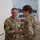 USARIEM COC/Relinquishment of Responsibility 2026 A U.S. Army military ceremony is taking place in what appears to be an indoor facility. A soldier identified by name tape as 'MARCONI,' wearing a Sergeant First Class rank insignia and a medal on his chest, is shaking hands with a female officer in U.S. Army OCP (Operational Camouflage Pattern) uniform. A third soldier holds what appears to be a certificate or award document, suggesting this is a formal recognition or award ceremony.
