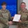 USARIEM COC/Relinquishment of Responsibility 2026 Two U.S. Army soldiers are posing together while shaking hands and jointly holding a certificate in a formal recognition ceremony. The soldier on the left, identified by a name tape reading 'JENKINS' and wearing a single star indicating Brigadier General rank, is presenting the award. The soldier on the right, whose name tape appears to read 'MARCONI' or similar, is wearing a medal on their chest, suggesting this is a retirement or commendation ceremony.