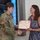 USARIEM COC/Relinquishment of Responsibility 2026 A U.S. Army soldier in OCP (Operational Camouflage Pattern) uniform is presenting a Certificate of Appreciation to a civilian woman. The two individuals are shaking hands while jointly holding the certificate. The ceremony appears to be taking place indoors in front of a large display screen.