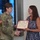 USARIEM COC/Relinquishment of Responsibility 2026 A U.S. Army soldier in OCP (Operational Camouflage Pattern) uniform is presenting a Certificate of Appreciation to a civilian woman in a blue floral dress. The two individuals are shaking hands while jointly holding the framed certificate. The ceremony appears to be taking place indoors in a modern facility.