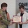 USARIEM COC/Relinquishment of Responsibility 2026 A U.S. Army officer in camouflage uniform is presenting a certificate to a young civilian man during what appears to be a formal recognition ceremony. The certificate is from 'The United States Army B·R·A·T' program and is made out to 'Joseph A. Marconi'. The event is taking place indoors in front of a wall with text reading 'ONE TEAM' and phrases about advancing innovative technology.