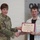 USARIEM COC/Relinquishment of Responsibility 2026 A U.S. Army soldier in camouflage uniform is presenting a certificate to a civilian male during what appears to be a formal recognition ceremony. The certificate is from the United States Army B.R.A.T. program and is made out to 'Joseph A. Marconi'. A civilian woman stands in the background observing the presentation.