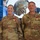 USARIEM COC/Relinquishment of Responsibility 2026 Two U.S. Army soldiers in MultiCam/OCP camouflage uniforms are posing together in front of a large digital display screen showing military helmet technology. Both soldiers are wearing red-and-white medals on their chests, indicating a formal recognition or awards ceremony. Their name tapes read 'ROSSER' (left) and 'MARCONI' (right).