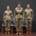 USARIEM COC/Relinquishment of Responsibility 2026 Three U.S. Army soldiers in Operational Camouflage Pattern (OCP) uniforms stand at attention on a stage during what appears to be a formal military ceremony. The center soldier is distinguished by a ceremonial belt with a gold buckle, suggesting a position of command or special recognition. An audience member in civilian clothing is partially visible in the foreground.