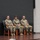 USARIEM COC/Relinquishment of Responsibility 2026 Three U.S. Army soldiers in OCP (Operational Camouflage Pattern) uniforms are seated on a stage during what appears to be a formal military ceremony or event. Two appear to be female and one male, all seated in blue upholstered chairs on a wooden stage. A maroon/burgundy military unit guidon or flag is visible to the left.