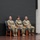 USARIEM COC/Relinquishment of Responsibility 2026 Three U.S. Army soldiers in OCP (Operational Camouflage Pattern) uniforms are seated on a stage during what appears to be a formal military ceremony. Two appear to be female and one male, seated in matching blue leather chairs on a wooden stage. A maroon/burgundy military unit guidon flag is visible on the left side of the stage.