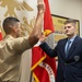 A military enlistment or oath-of-office ceremony is taking place at what appears to be a Marine Corps recruiting station. A Marine in service uniform administers an oath to a young civilian man in a navy blazer, both with right hands raised. The setting includes American and Marine Corps flags, and a 'Poolee' board visible on the wall in the background.