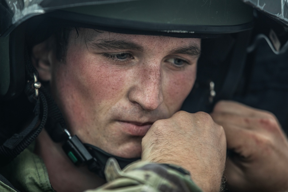A close-up portrait of a young male soldier wearing a military helmet and multicam/camouflage uniform. His fist is raised near his chin, and he appears focused or in a moment of concentration or fatigue. The image is a high-quality, dramatic military portrait with shallow depth of field.