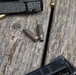 The image shows multiple rifle cartridges and spent brass casings scattered on a weathered wooden surface. A Federal Cartridge ammunition box is partially visible in the upper left corner, along with what appears to be a firearm magazine in the lower right. Two of the casings in the center appear to be fired/spent, showing deformation at the mouth.