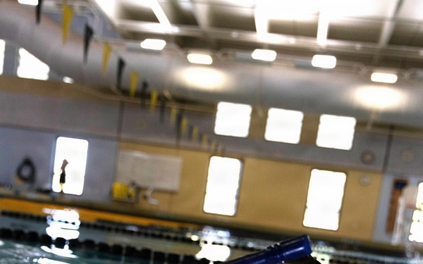 A person is swimming in an indoor pool while using a blue snorkel. The camera angle is at water level, providing a close-up view of the swimmer's face and the snorkel equipment. The setting appears to be a recreational or training indoor aquatic facility.