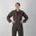 A female military aviator stands in a confident pose with hands on hips against a neutral white/grey background. She is wearing an olive green flight suit with visible unit patch and name tag, consistent with U.S. Marine Corps aviation attire. The image appears to be an official or semi-official portrait photograph.
