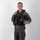 MCAS Marines pose for content 2026 A young male military aviator stands in a full-body portrait pose against a plain white/light gray studio backdrop. He is wearing a complete flight suit ensemble with survival/tactical vest, harness, and is holding a flight helmet. The image appears to be a professional or official military portrait photograph.