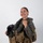 MCAS Marines pose for content 2026 A smiling individual is posed against a plain white background wearing full military aviation flight gear, including a tactical vest and flight suit. They are holding a flight helmet with an attached oxygen mask and night vision goggle mount. The image appears to be a professional portrait or official military photo.