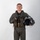 MCAS Marines pose for content 2026 A young male military aviator stands in a formal portrait pose against a plain white/grey studio background. He is wearing a full flight suit ensemble with survival vest and harness, holding a flight helmet in his right hand. The image appears to be an official or professional military portrait photograph.