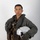 MCAS Marines pose for content 2026 A military aviator poses against a neutral white/gray background in a formal portrait-style photograph. The individual is wearing a full flight suit ensemble including a survival vest, harness system, and is holding a white flight helmet. The image appears to be an official military portrait.