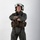 MCAS Marines pose for content 2026 A military aviator stands in a full-body portrait pose against a white studio background with arms crossed. The individual is wearing a complete flight suit ensemble including a flight helmet, survival vest, and harness system. The image appears to be a professional or official military portrait photograph.