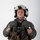 MCAS Marines pose for content 2026 A military aviator or aircrew member is photographed against a plain white background in a formal portrait-style image. The individual is wearing full flight gear including a flight suit, survival vest, flight helmet, and gloves. The image appears to be an official or semi-official military portrait.