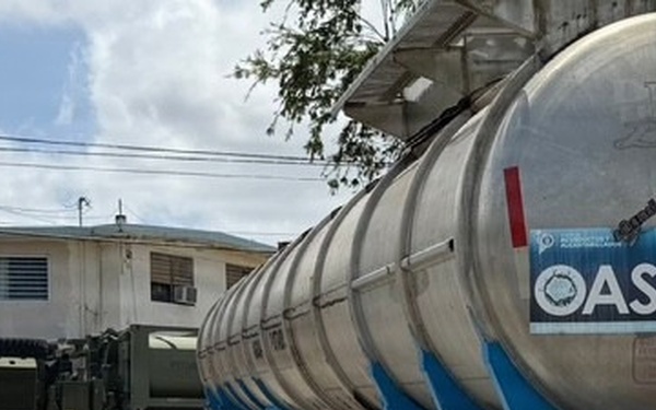 Military Vehicle and Oasis Water Tanker Operate Near Residential Building During Water Distribution Mission