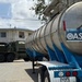 Military Vehicle and Oasis Water Tanker Operate Near Residential Building During Water Distribution Mission