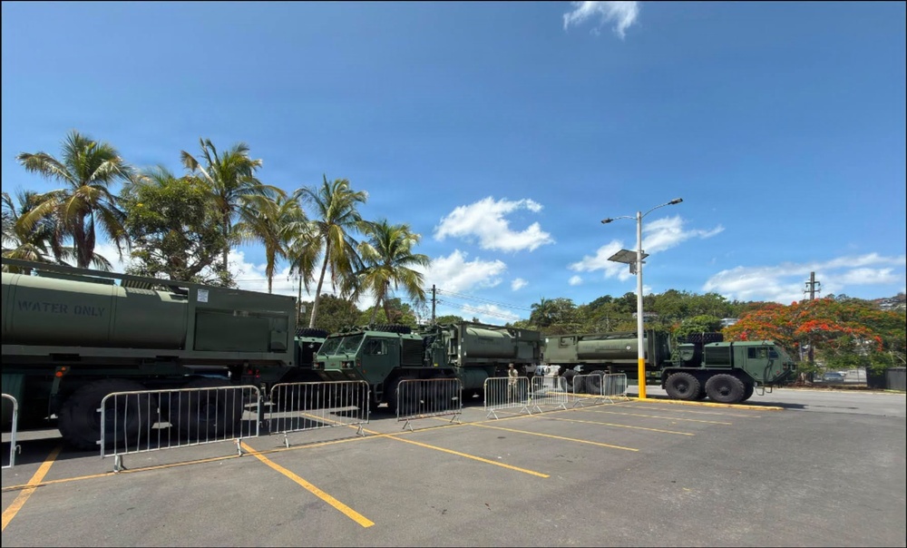 Military Water Trucks Staged in Tropical Parking Lot Behind Security Barriers