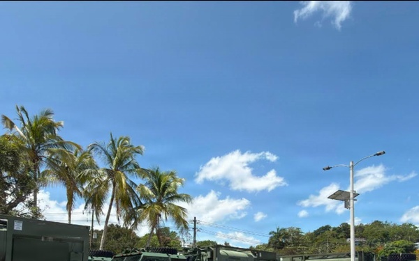 Military Water Trucks Staged in Tropical Parking Lot Behind Security Barriers