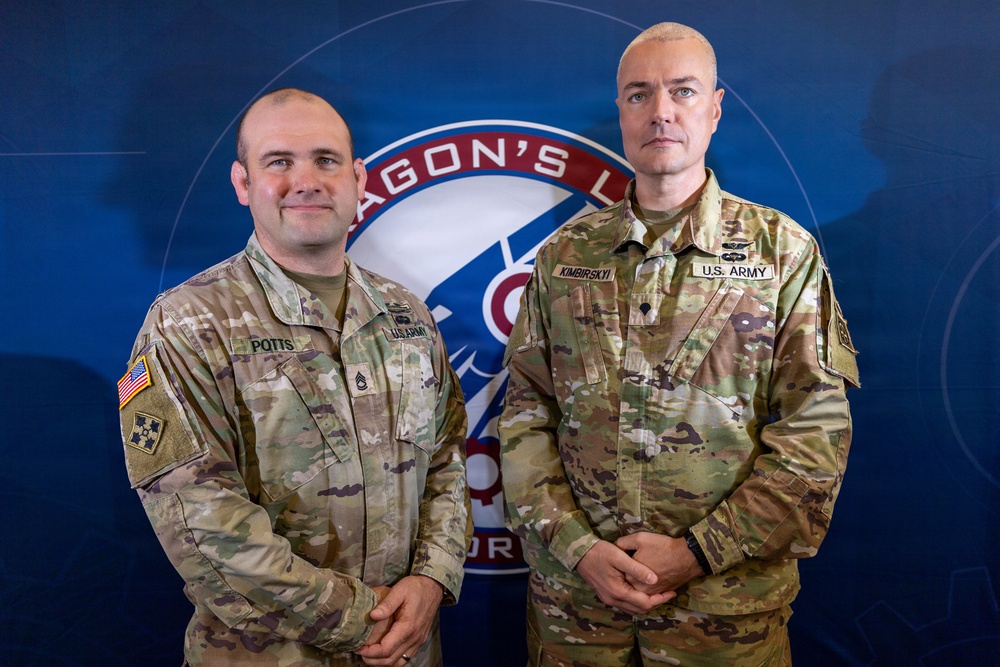 Two U.S. Army soldiers in OCP (Operational Camouflage Pattern) uniforms pose for a formal photo in front of a blue backdrop featuring a military unit insignia partially reading 'AGON'S L' (likely 'Dragon's Lair' or similar). The soldier on the left is identified by name tape as 'POTTS' and the soldier on the right as 'KIMBIRSKYI', both wearing U.S. Army name tapes. The image appears to be an official military portrait or recognition photo.