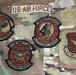 The image shows a U.S. Air Force OCP (Operational Camouflage Pattern) uniform with multiple embroidered patches displayed. Four circular intelligence squadron patches and one shield-shaped command patch are visible, along with a 'U.S. AIR FORCE' tape. The patches are associated with intelligence squadrons and Air Force Reserve Command.