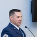 A U.S. Air Force Senior Master Sergeant named Ehlert is speaking at a podium, wearing the Air Force Service Dress uniform. He is gesturing with his right hand while addressing an audience, suggesting a formal ceremony or official presentation. His rank insignia and name tag are clearly visible on his uniform.