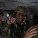Several military personnel in camouflage uniforms and tactical helmets are seated inside what appears to be a military aircraft or helicopter. At least one individual displays a red cross medical patch, suggesting the presence of a combat medic. The personnel appear to be in transit or preparing for an operation.