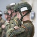 The image shows a line of military personnel wearing German Bundeswehr flecktarn camouflage uniforms and tactical helmets. The foreground soldier's helmet bears a label reading 'Team Number 6' and 'Helmet Number 6.4', suggesting a structured military exercise or competition. German flag patches are visible on the soldiers' sleeves, confirming their national affiliation.