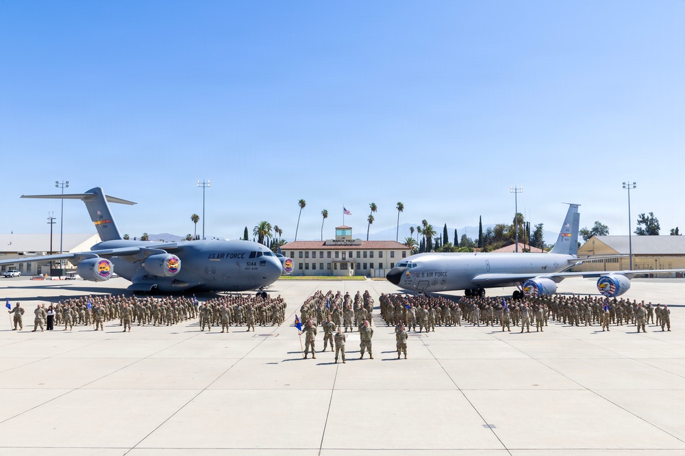 A large group of U.S. Air Force personnel are assembled on a flight line apron at March Field Air Reserve Base in California, posing for a formal group photograph. Two U.S. Air Force aircraft are prominently displayed — a C-17 Globemaster III on the left (tail number 5144) and a KC-135 Stratotanker on the right — both bearing colorful unit insignia. The historic March Field administration building with a flagpole flying the American flag is visible in the background.