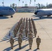 A formal military formation photograph taken on the flight line at March Field (March Air Reserve Base), California. Personnel in OCP (Operational Camouflage Pattern) uniforms are arranged in precise rows between two U.S. Air Force aircraft. A guidon bearer stands at the front-left of the formation alongside what appear to be senior officers or NCOs.
