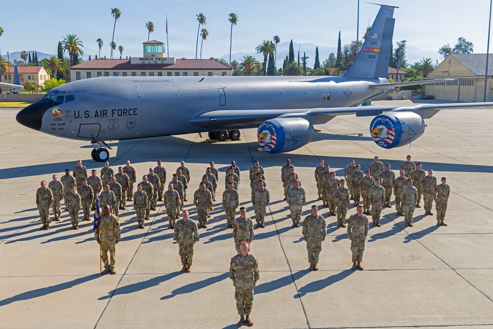A formal military group photograph taken on the flight line at March Field Air Reserve Base, featuring a large formation of U.S. Air Force personnel in OCP (Operational Camouflage Pattern) uniforms. A KC-135 Stratotanker aircraft bearing the markings '452 AMW' (Air Mobility Wing) and unit insignia is prominently displayed behind the formation. The building in the background is labeled 'MARCH FIELD,' identifying this as March Air Reserve Base in Riverside, California.