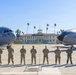 Eight U.S. Air Force personnel in OCP (Operational Camouflage Pattern) uniforms are posed on a flight line at March Air Reserve Base (March Field) in California. Two large U.S. Air Force aircraft are positioned on either side of the group, with the historic March Field headquarters building visible in the background. The aircraft markings indicate assignment to the 452nd Air Mobility Wing.