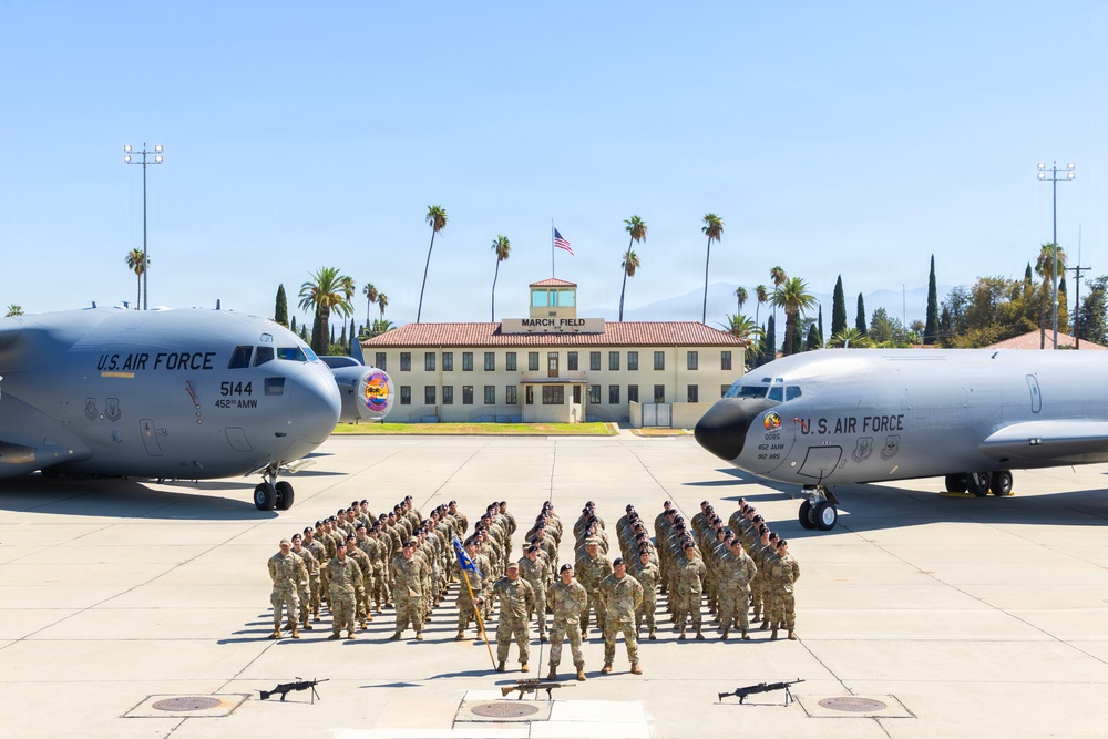 A formal military unit photograph taken on the flight line at March Field Air Reserve Base, showing a large formation of uniformed personnel posed between two U.S. Air Force aircraft. The building in the background is clearly labeled 'MARCH FIELD' and displays an American flag. Two aircraft bearing '452nd AMW' (Air Mobility Wing) markings flank the formation symmetrically.