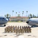 A formal military unit photograph taken on the flight line at March Field Air Reserve Base, showing a large formation of uniformed personnel posed between two U.S. Air Force aircraft. The building in the background is clearly labeled 'MARCH FIELD' and displays an American flag. Two aircraft bearing '452nd AMW' (Air Mobility Wing) markings flank the formation symmetrically.