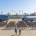 A large U.S. Air Force unit formation photograph taken on a flight line at March Field (March Air Reserve Base), California. Military personnel in camouflage uniforms are arranged in formal parade formation between two U.S. Air Force aircraft. The scene includes a C-17 Globemaster III on the left and a KC-135 Stratotanker on the right, with the historic March Field building visible in the background.