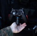 A person wearing U.S. Marine Corps MARPAT digital camouflage is holding a specialized military vehicle control unit in the palm of their hand. The device resembles a gamepad-style controller but is labeled with vehicle operation functions such as 'Horn,' 'Park,' 'Neutral,' 'Drive,' 'Steer,' and 'Lock.' It appears to be a remote or direct-interface controller for a military ground vehicle.